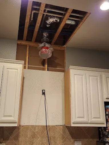 Opened ceiling above kitchen cabinets with a worker on a ladder